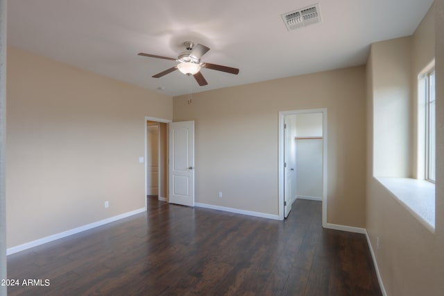 unfurnished bedroom with ceiling fan, a closet, dark wood-type flooring, and a spacious closet