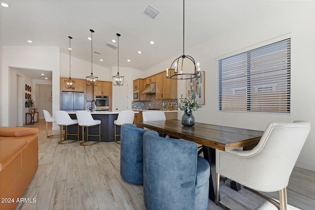 dining area featuring an inviting chandelier, light hardwood / wood-style floors, vaulted ceiling, and sink