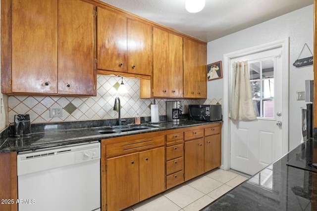 kitchen with light tile patterned flooring, sink, dark stone countertops, and white dishwasher