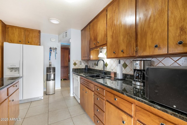 kitchen featuring sink, light tile patterned floors, white appliances, dark stone counters, and backsplash