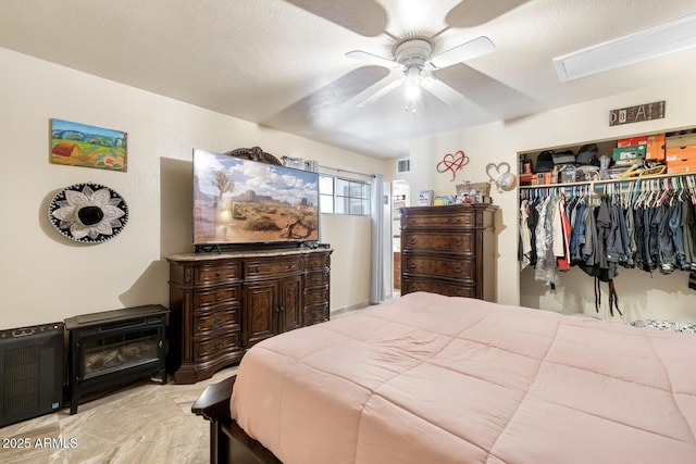 bedroom with a textured ceiling, a closet, ceiling fan, and a wood stove