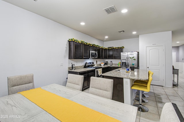 kitchen featuring a breakfast bar, light stone counters, light tile patterned floors, an island with sink, and stainless steel appliances