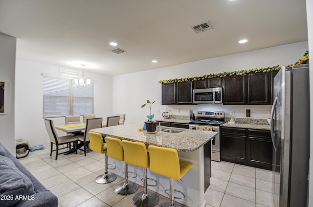 kitchen with a breakfast bar, hanging light fixtures, stainless steel appliances, an island with sink, and light tile patterned flooring