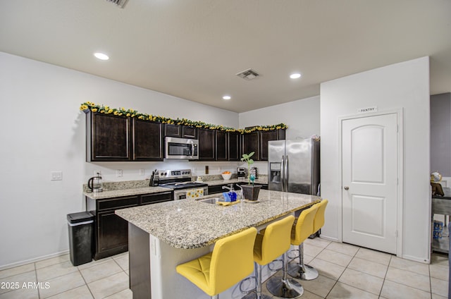 kitchen with sink, a breakfast bar area, a kitchen island with sink, stainless steel appliances, and dark brown cabinets