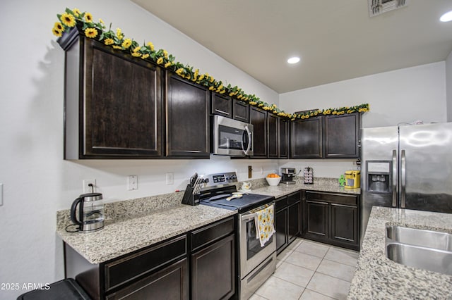 kitchen featuring light tile patterned floors, sink, stainless steel appliances, dark brown cabinetry, and light stone countertops