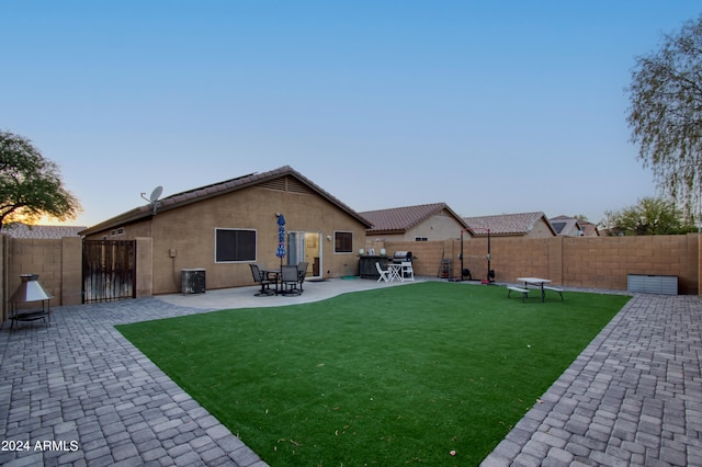 back house at dusk featuring a patio and a lawn