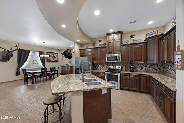 1008 E Mano Dr, New River, AZ 85087 - kitchen with stainless steel appliances, a sink, a kitchen bar, backsplash, and a chandelier