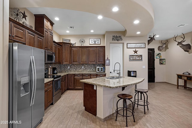 1008 E Mano Dr, New River, AZ 85087 - kitchen with appliances with stainless steel finishes, a sink, light wood-style flooring, a kitchen bar, and decorative backsplash