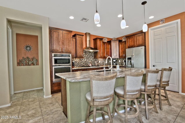 kitchen with decorative light fixtures, stainless steel appliances, decorative backsplash, wall chimney range hood, and a kitchen bar