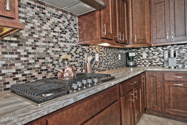 kitchen featuring tasteful backsplash, stainless steel gas stovetop, wall chimney range hood, and light tile patterned floors