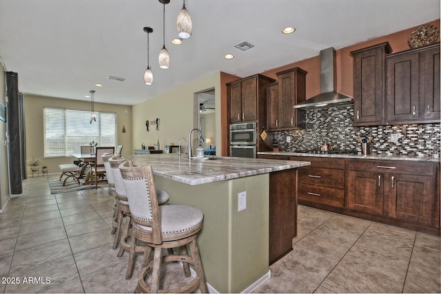 kitchen featuring a sink, wall chimney range hood, decorative backsplash, and light tile patterned floors