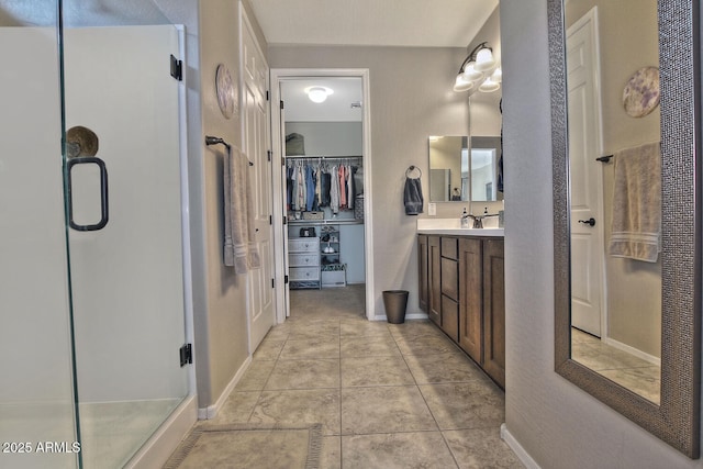 full bathroom featuring vanity, baseboards, a shower stall, tile patterned floors, and a walk in closet