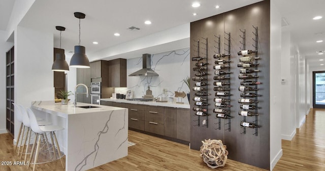 kitchen with visible vents, modern cabinets, light wood-style floors, appliances with stainless steel finishes, and wall chimney exhaust hood