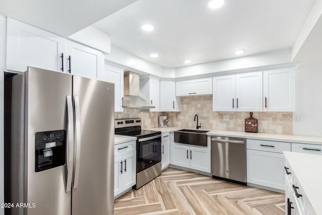 kitchen featuring wall chimney exhaust hood, stainless steel appliances, light parquet floors, sink, and white cabinetry