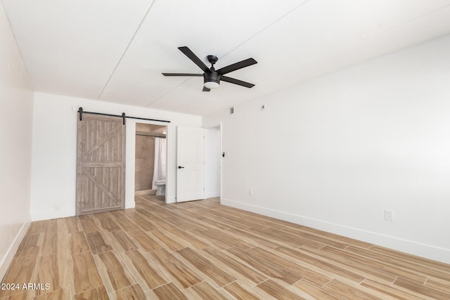 unfurnished bedroom featuring hardwood / wood-style flooring, ceiling fan, a barn door, and connected bathroom