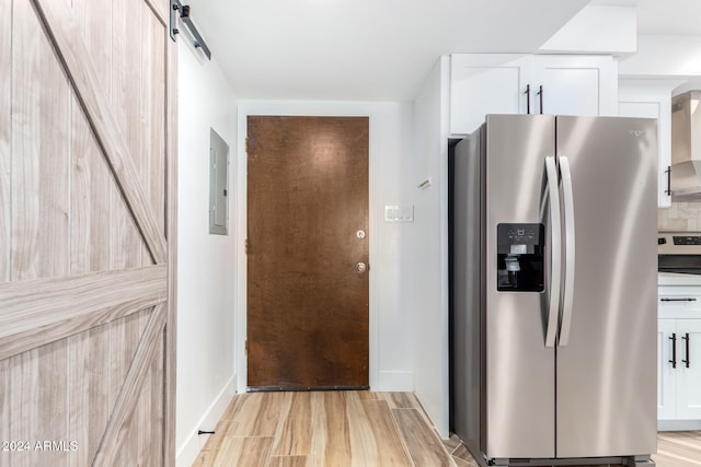 kitchen featuring white cabinets, wall chimney exhaust hood, a barn door, light wood-type flooring, and stainless steel fridge with ice dispenser