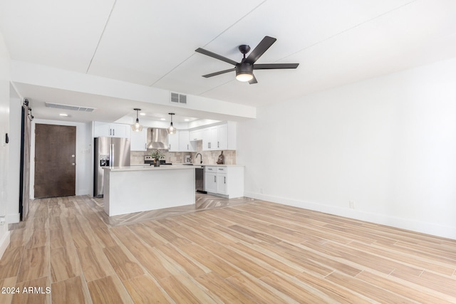 unfurnished living room featuring a barn door, light hardwood / wood-style floors, ceiling fan, and sink