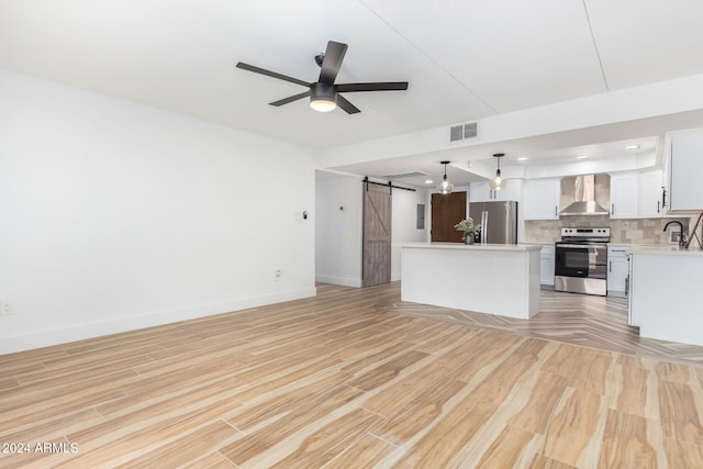 unfurnished living room with a barn door, light hardwood / wood-style floors, ceiling fan, and sink