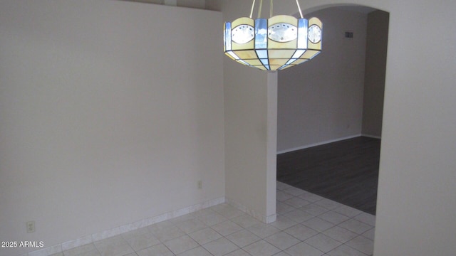 unfurnished dining area with light tile patterned floors, baseboards, arched walkways, and a notable chandelier