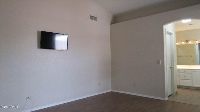 unfurnished bedroom with visible vents, light wood-style flooring, ensuite bathroom, arched walkways, and baseboards