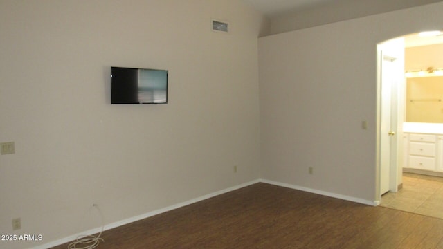 spare room featuring wood finished floors, visible vents, baseboards, arched walkways, and vaulted ceiling