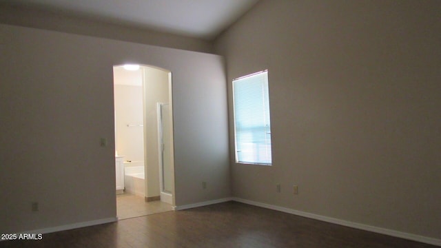 unfurnished bedroom with connected bathroom, wood finished floors, arched walkways, and baseboards