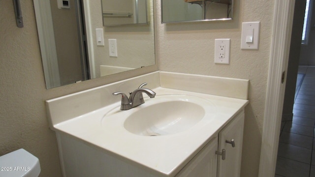bathroom featuring toilet, vanity, and a textured wall