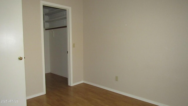 unfurnished bedroom with a closet, a walk in closet, baseboards, and wood finished floors