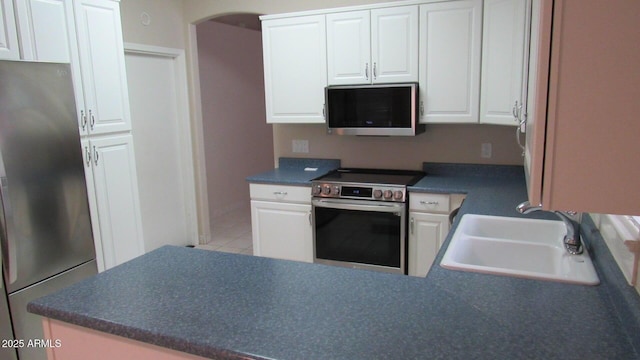 kitchen featuring a sink, arched walkways, appliances with stainless steel finishes, and white cabinets