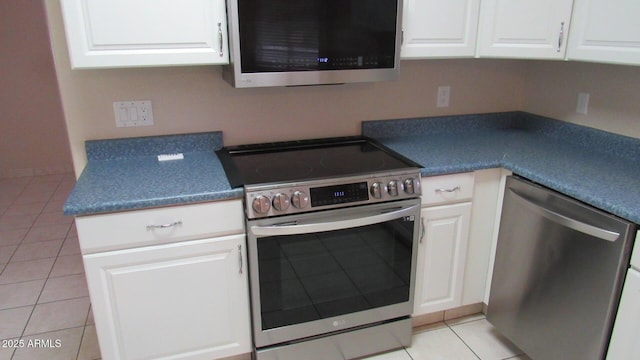 kitchen featuring light tile patterned floors, white cabinets, stainless steel appliances, and dark countertops
