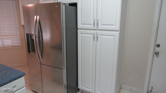 kitchen featuring light tile patterned floors, baseboards, white cabinets, dark countertops, and stainless steel fridge