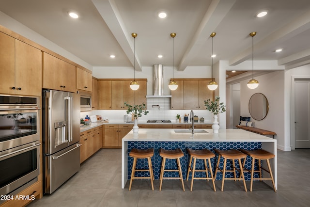 kitchen featuring appliances with stainless steel finishes, a sink, wall chimney range hood, beamed ceiling, and a kitchen breakfast bar