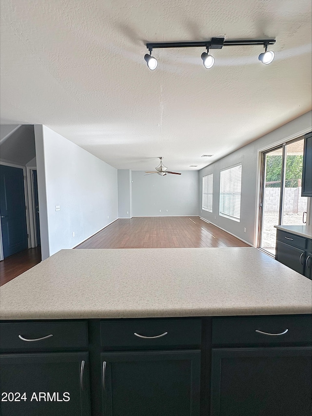 kitchen with ceiling fan, rail lighting, wood-type flooring, and a textured ceiling