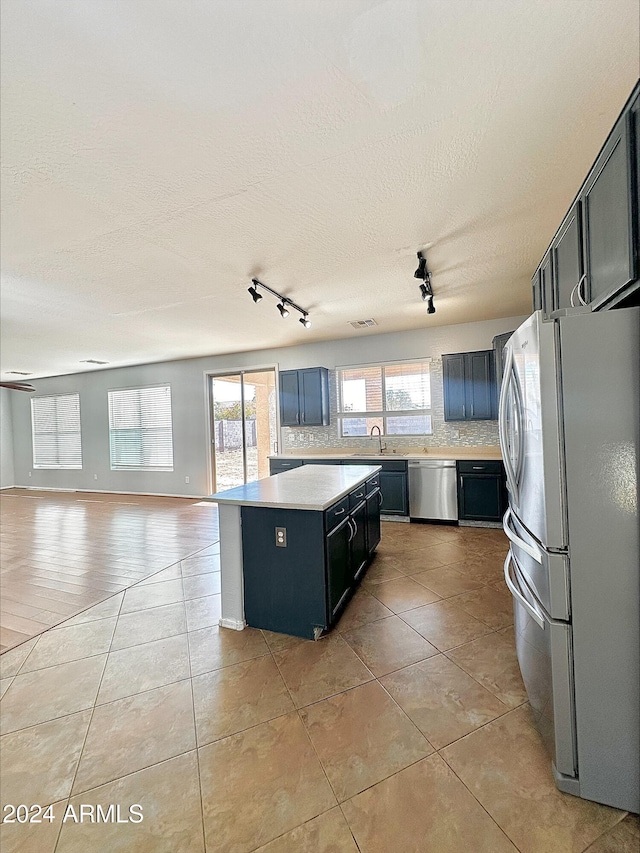 kitchen with appliances with stainless steel finishes, track lighting, sink, a center island, and light tile patterned flooring