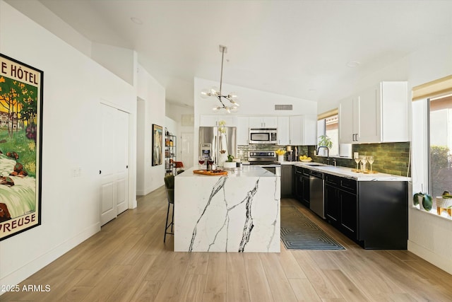 kitchen featuring appliances with stainless steel finishes, dark cabinets, decorative light fixtures, a center island, and white cabinetry