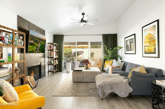 living area with a warm lit fireplace, a ceiling fan, vaulted ceiling, and light wood finished floors