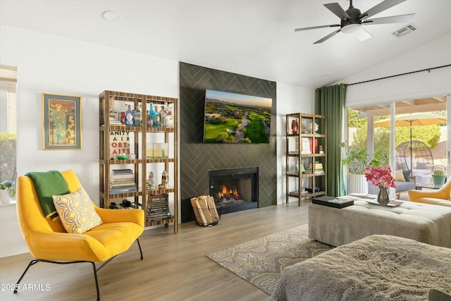 living area with light wood finished floors, visible vents, a ceiling fan, vaulted ceiling, and a fireplace