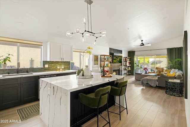 kitchen with white cabinets, a kitchen island, decorative light fixtures, light stone countertops, and a sink