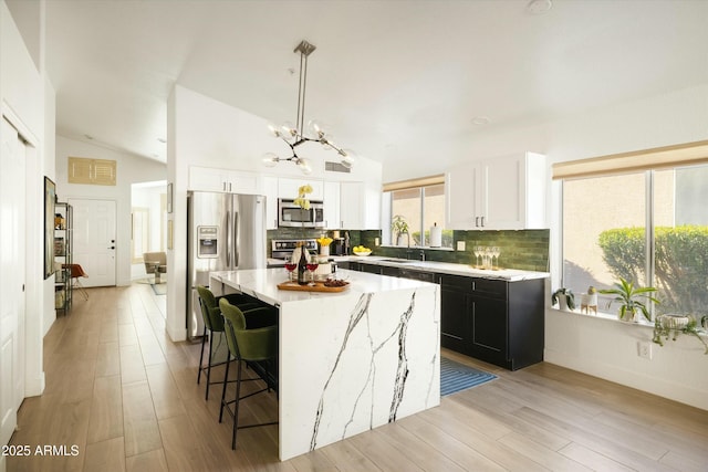 kitchen with white cabinets, a center island, hanging light fixtures, stainless steel appliances, and a sink