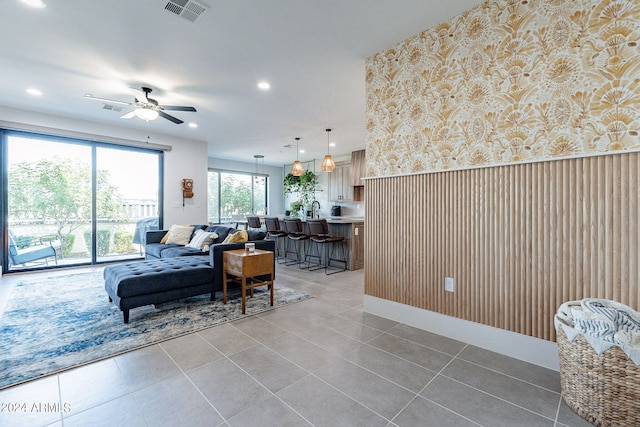 living room with ceiling fan, wood walls, sink, and tile patterned floors