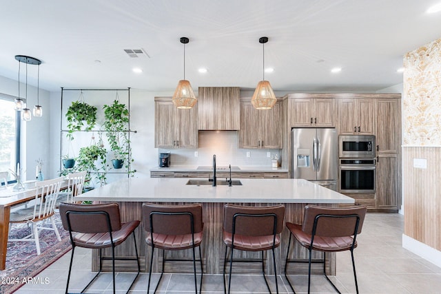 kitchen with stainless steel appliances, a center island with sink, decorative light fixtures, and sink