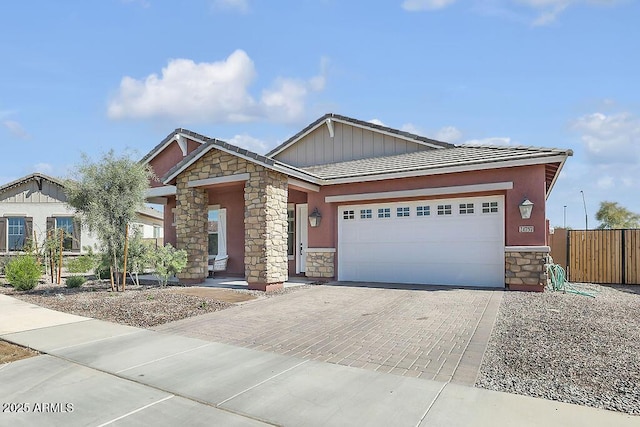 craftsman-style house featuring a garage, stone siding, fence, and decorative driveway