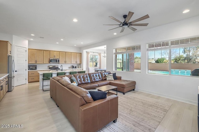 living area featuring recessed lighting, baseboards, light wood finished floors, and ceiling fan with notable chandelier