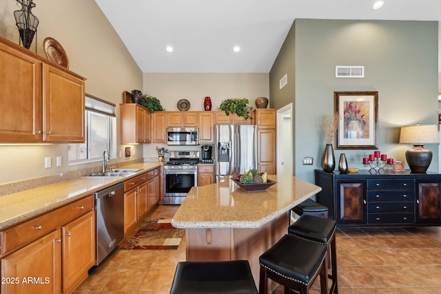 kitchen featuring a kitchen island, sink, a kitchen breakfast bar, light stone counters, and stainless steel appliances