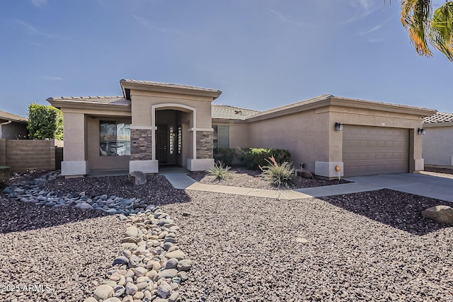 prairie-style home featuring stucco siding, concrete driveway, an attached garage, fence, and stone siding