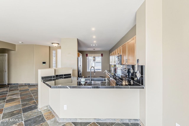 kitchen featuring stone tile floors, stainless steel appliances, visible vents, a sink, and a peninsula