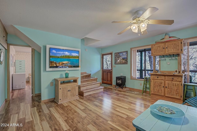 living room with a wood stove, ceiling fan, plenty of natural light, and light hardwood / wood-style floors