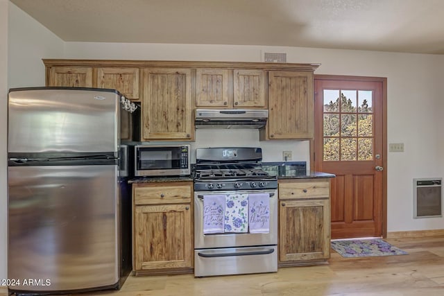 kitchen with dark stone counters, fume extractor, light hardwood / wood-style flooring, and appliances with stainless steel finishes