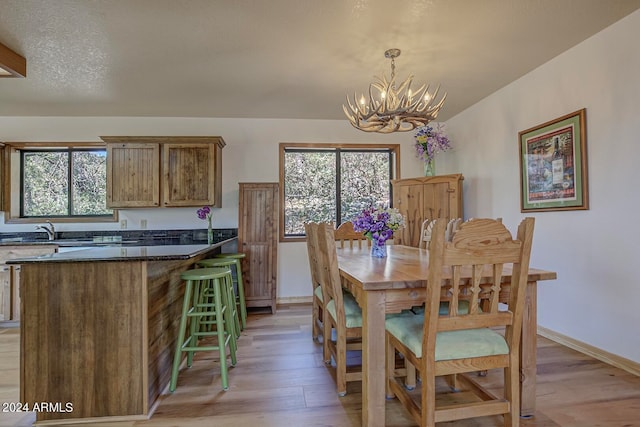 dining area featuring sink, a healthy amount of sunlight, light wood-type flooring, and an inviting chandelier