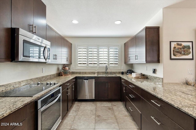 kitchen with sink, light stone counters, a textured ceiling, light tile patterned floors, and stainless steel appliances